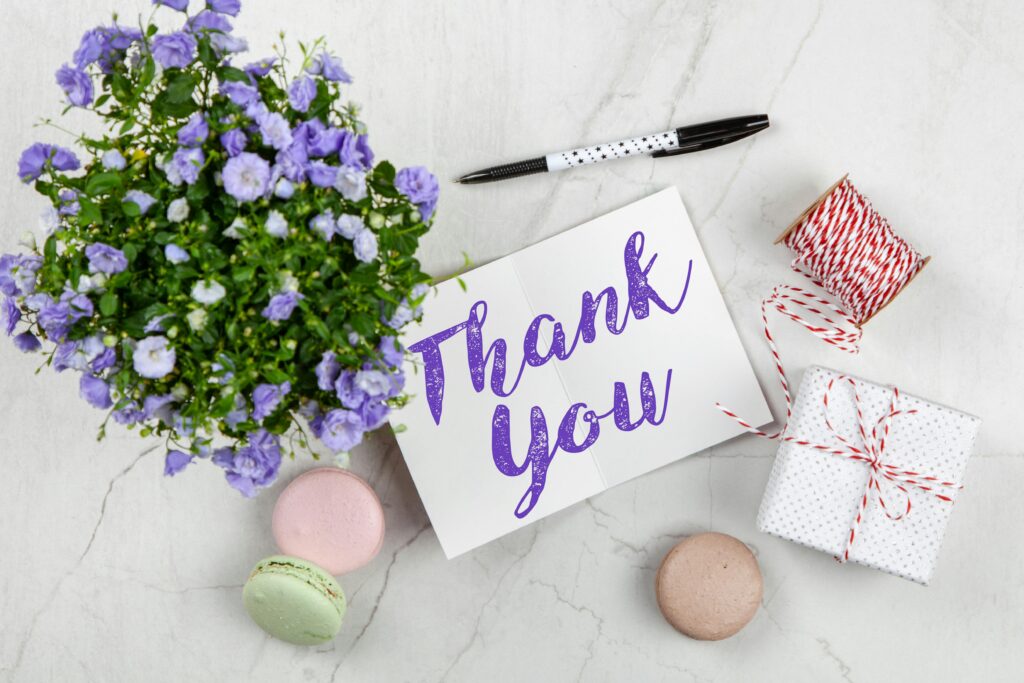 Opticlikks -An elegant thank you card with flowers and a gift on a marble surface, perfect for expressing gratitude.